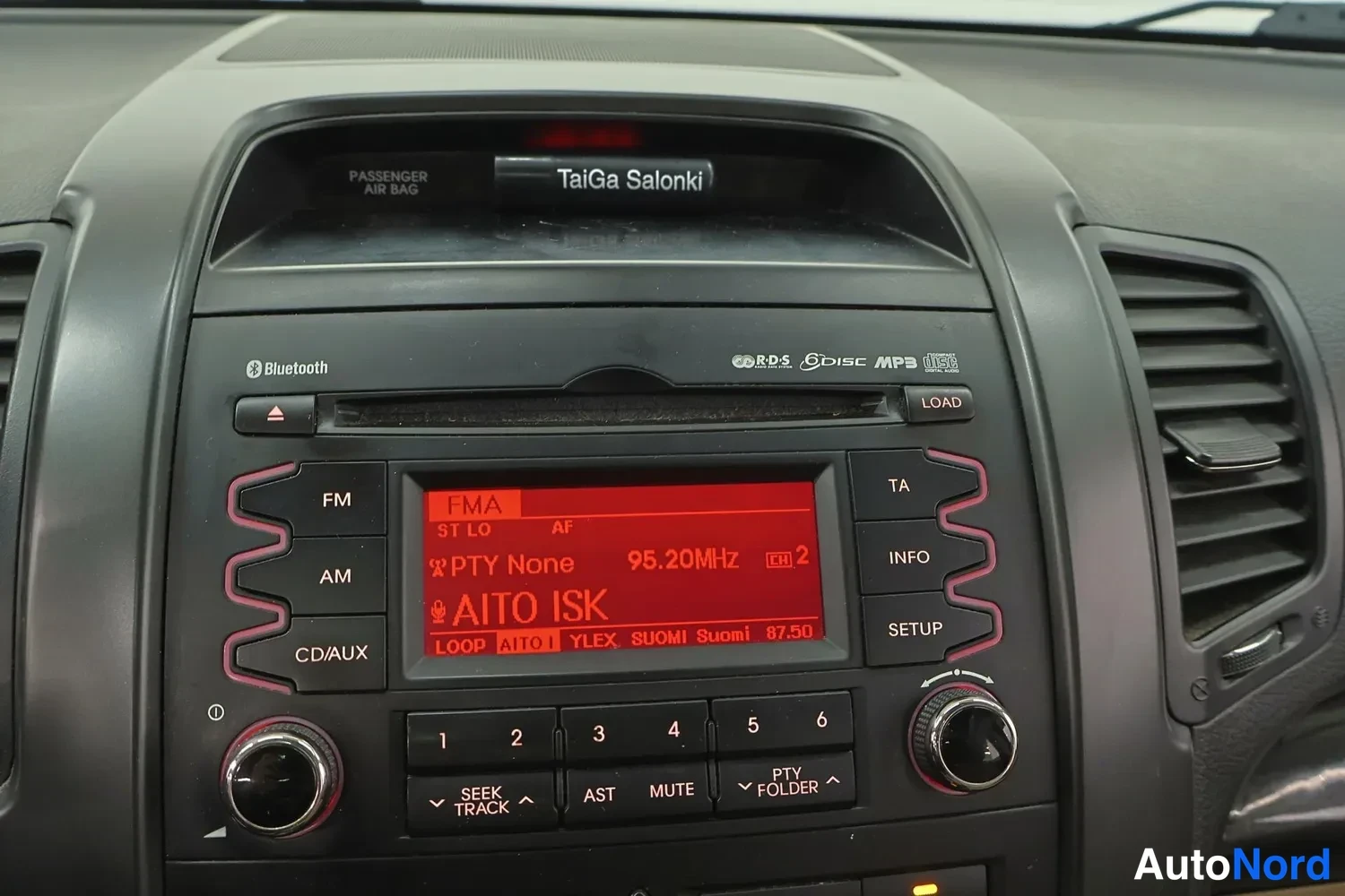 Muu: Kojelaudan keskiosa: radio- ja CD-laite Bluetooth-merkinnällä, näytössä FMA 95.20 MHz AITO ISK ja viereinen TaiGa Salonki -kilpi.