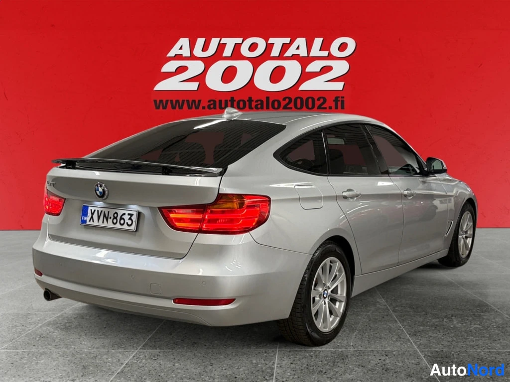 Takaviisto: Hopeanvärinen BMW 3 Gran Turismo takaa vasemmalta kulmasta kuvattuna, rekisterikilpi, punainen tausta.