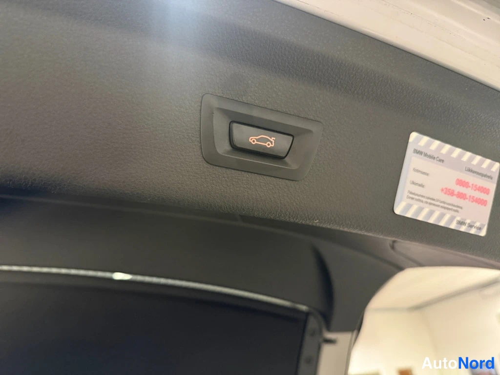 Muu: Takaluukun sähköinen avausnappi mustassa panelissa ja BMW Mobile Care -tarrta takaluukun sisäpinnassa.