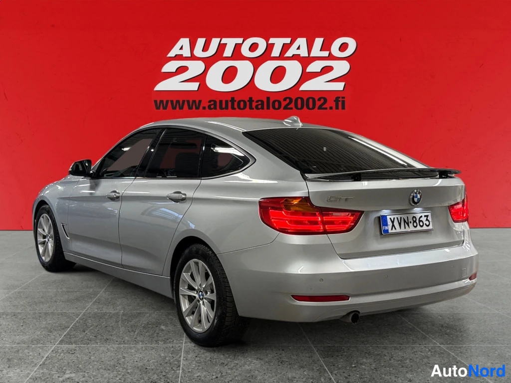 Takaviisto: Autotalo 2002 -kyltillä BMW 318 Gran Turismo takaa oikealta kuvattuna; rekisterikilpi lukee, sivuilta erottuvat ovenkahvat ja kattospoileri. Kori on hopeanvärin