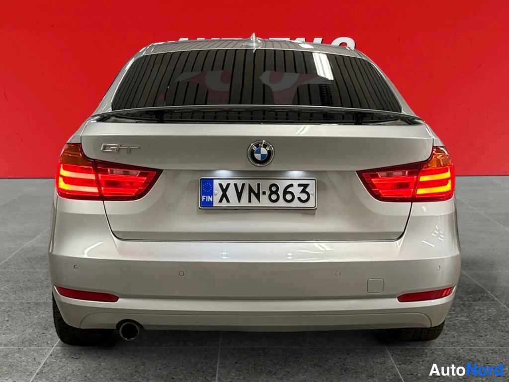 Takaa: Autotalo 2002 -kyltillä BMW 318 Gran Turismo suoraan takaa; takavaloissa valot päällä, kannessa GT-merkki ja BMW-logo, rekisterikilpi lukee. Kori on hopeanvärin