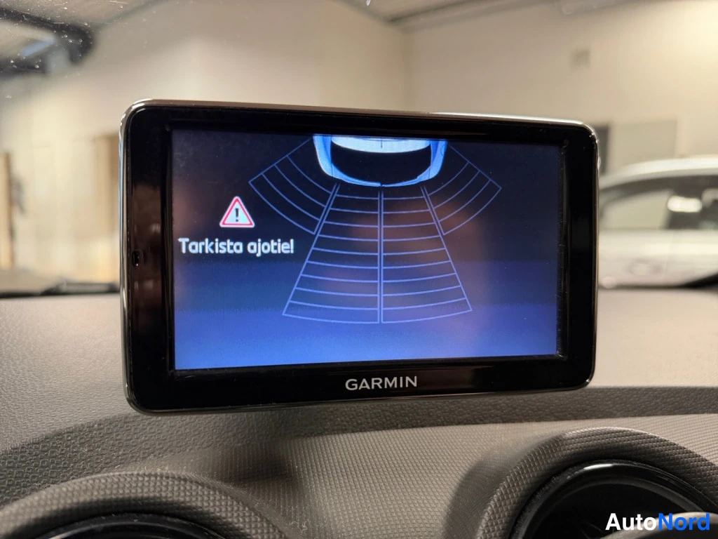 Muu: Kojelaudassa kiinnitetty Garmin-navigaattori, jonka näytössä on ilmoitus 'Tarkista ajotiet' ja varoituskolmio.