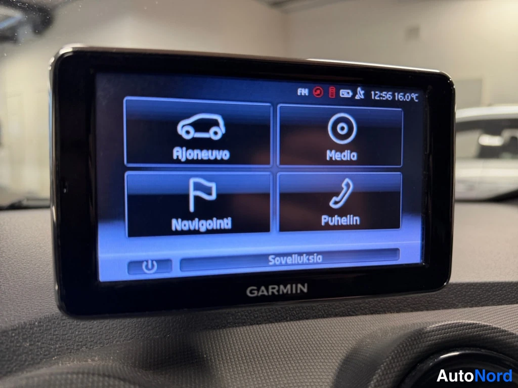 Yksityiskohta: Garmin-navigaattorin päävalikko kojelaudassa: vaihtoehdot Ajoneuvo, Media, Navigointi ja Puhelin, alareunassa Sovelluksia; aika 12:56 ja lämpötila 16,0 °C.