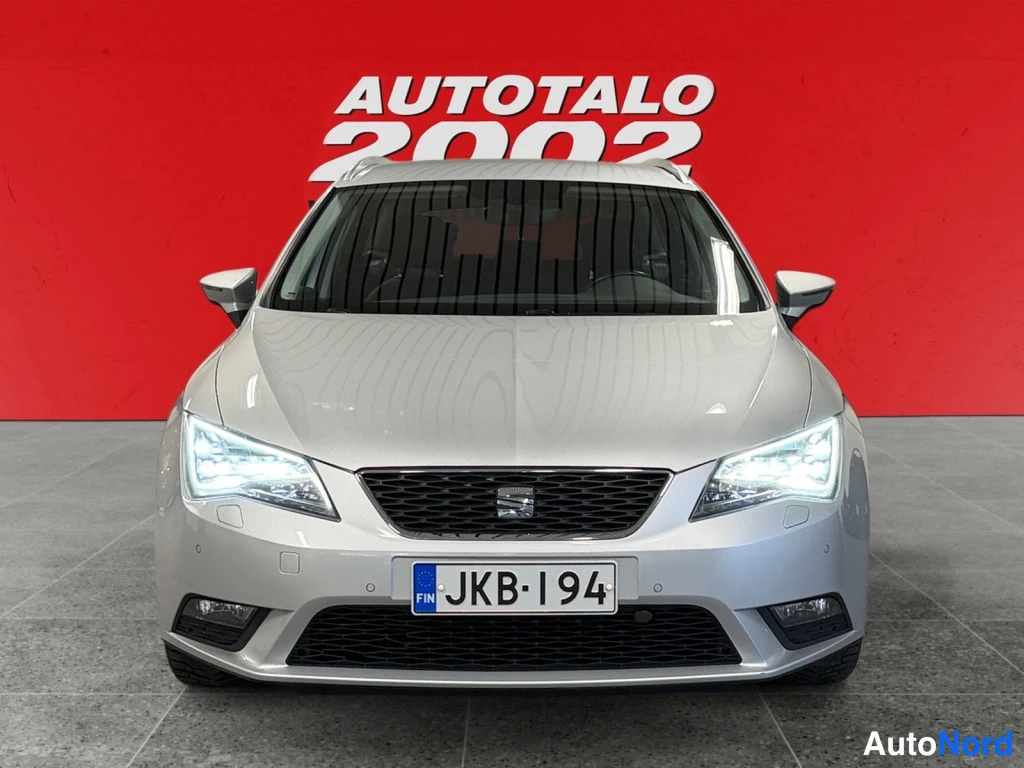 Edestä: Harmaa Seat Leon ST -farmari suoraan edestä kuvattuna; LED-ajovalot, Seat-merkki ja rekisteritunnus näkyvät.