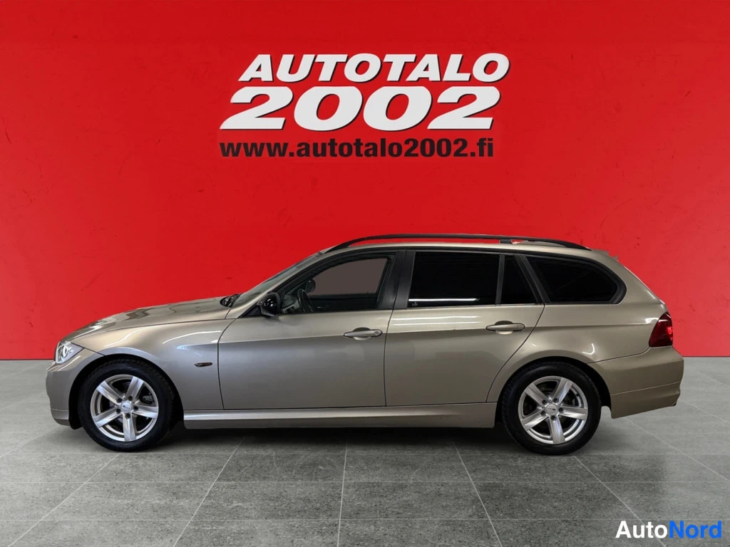 Etuviisto, nokka vasemmalle: Kulta/beige BMW 318 Touring -farmariauton sivukulma kulmassa, etuosa näkyvissä vasemmalla.