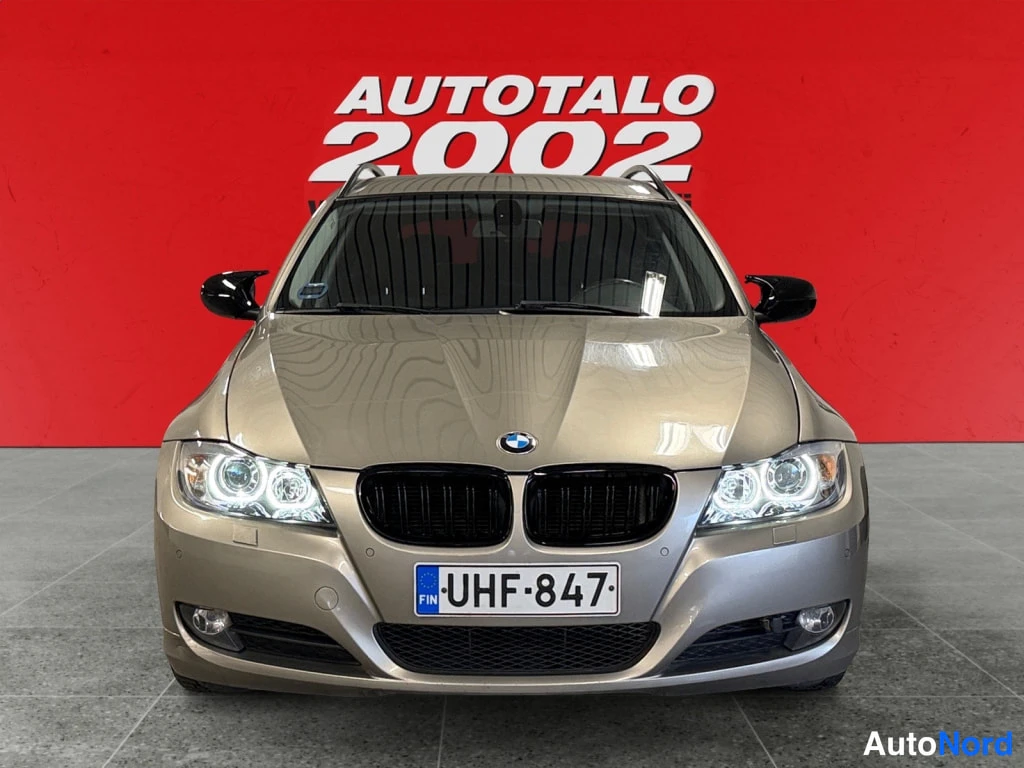 Edestä: Beige BMW 3:n etunäkymä suoraan edestä: mustat etusäleiköt, sumuvalot ja rekisterikilpi.
