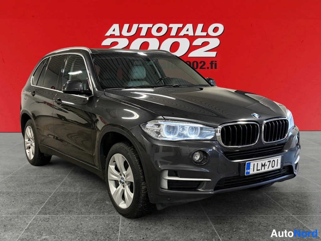 Etuviisto, nokka oikealle: Tummanharmaa BMW X5 -maastokuorma-auto kuvattu kolmannelta etukanamaiselta kulmalta, nokka osoittaa oikealle, näkyvissä etupyörä, keulakori ja etupyöräne