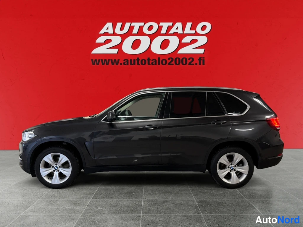 Etuviisto, nokka vasemmalle: Auton sivukuva kulmasta: tumma BMW X5, keulaa näkyy vasemmalla