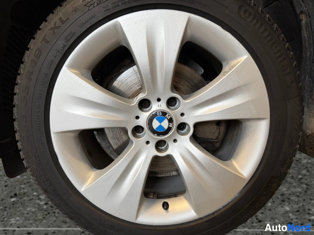 Yksityiskohta: Auton 19 tuuman hopeinen alumiinivanne BMW-merkillä, Continental-talvirenkaassa on näkyvissä merkinnät 235/55 R 19 TL ja.STUDDED.