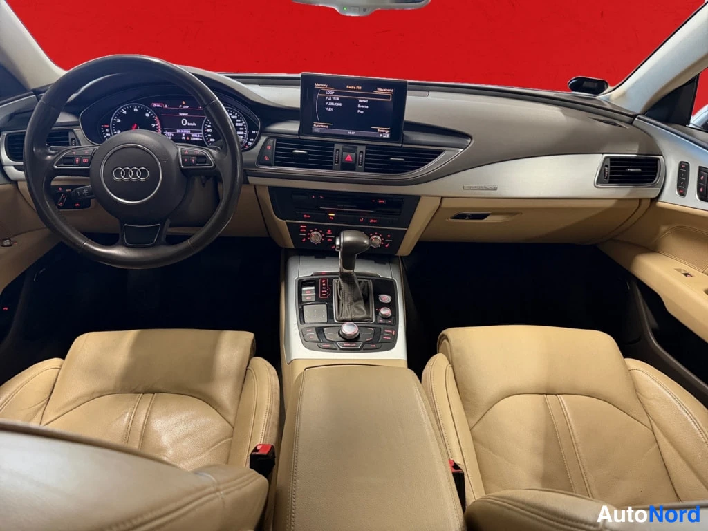 Sivulta: Audi A7:n kojelauta suoraan edestä: ohjauspyörä Audi-merkillä, mittaristo, MMI-näyttö ja automaattivaihteiston valitsin