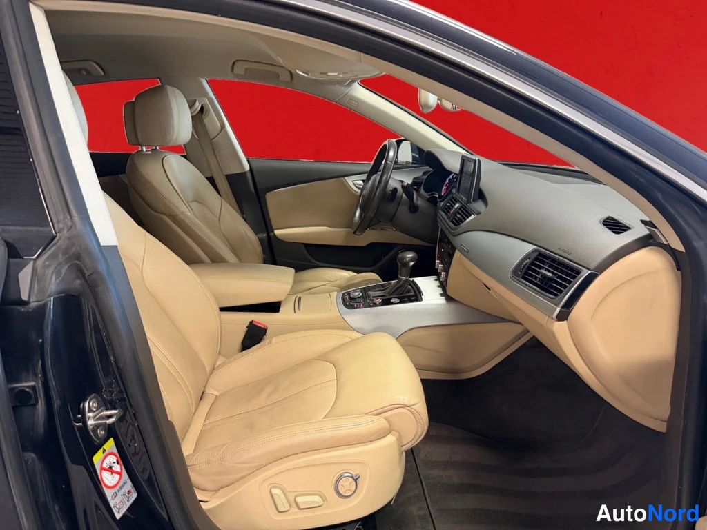 Edestä: Auton etupenkki ja kojelaudan alue beige-veroistuimin, ovista kuvattu sisätila; automaattivaihteen valitsin ja kosketusnäyttö näkyvät.
