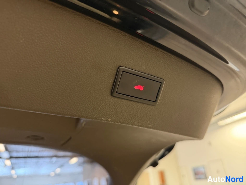 Edestä: Tavartilansisäluukun keskellä on sähkötoimisen takaluukun suljin painikkeella, punainen autonpaino puhelee.