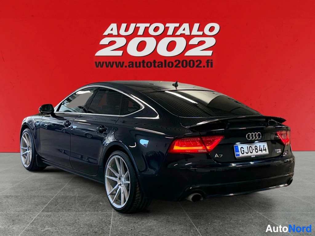 Takaviisto: Sinimustan Audi A7:n takaosa ja kylki punaisella taustalla, rekisteri, A7- ja TFSI-merkit.
