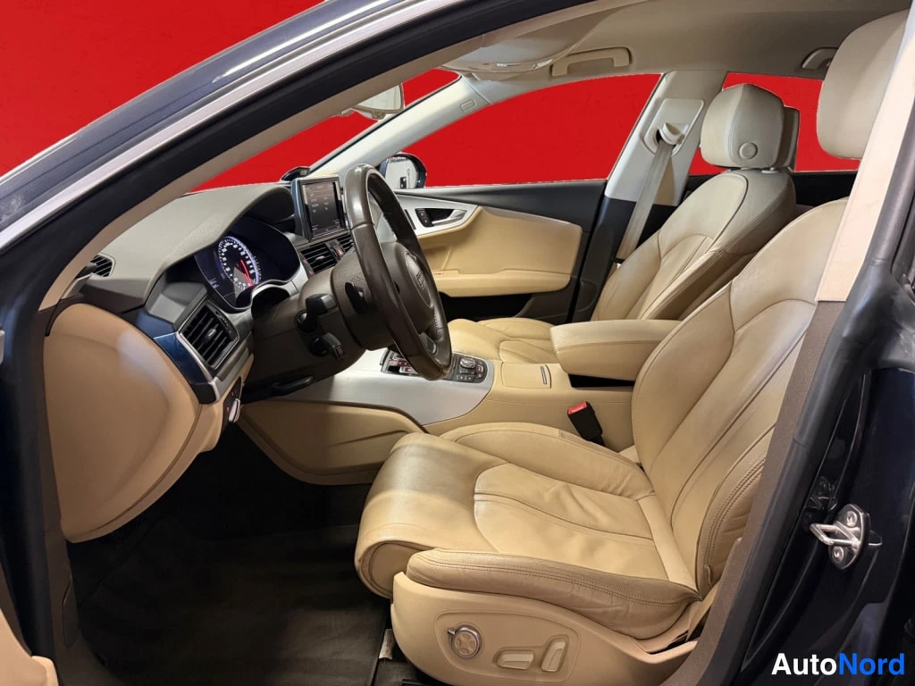 Sivulta: Audi A7:n matkustamo ohjaamosta oikealle: beige nahkapenkit, tumma ohjauspyörä ja kojelaudan näyttö