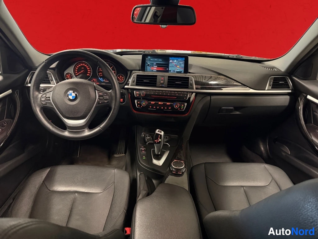 Yksityiskohta: Matkustamon yleiskuva konepeltäympäristöstä: BMW-ohjauspyörä, analogiset mittarit, automaattivaihteen valitsin ja näyttö jossa karttanäkymä.