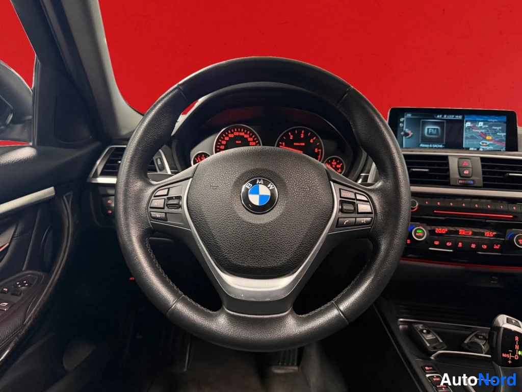 Muu: Sisätilakuva BMW:n ohjaamosta: musta kuljettajan matkustamon ympäristö, ohjauspyörä, analogiset mittarit ja keskinäytön navigointi.
