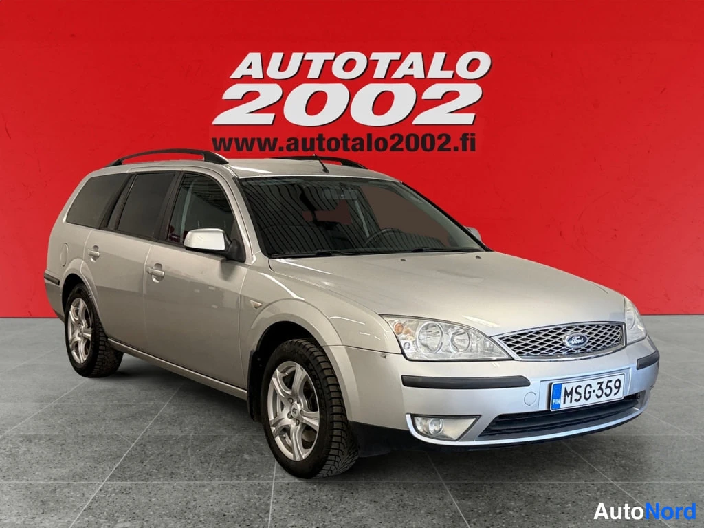 Etuviisto, nokka oikealle: Hopeanvärinen Ford Mondeo -farmari kuvattu etu-kolmasosakulmasta punaisella taustalla, rekisteritunnus.