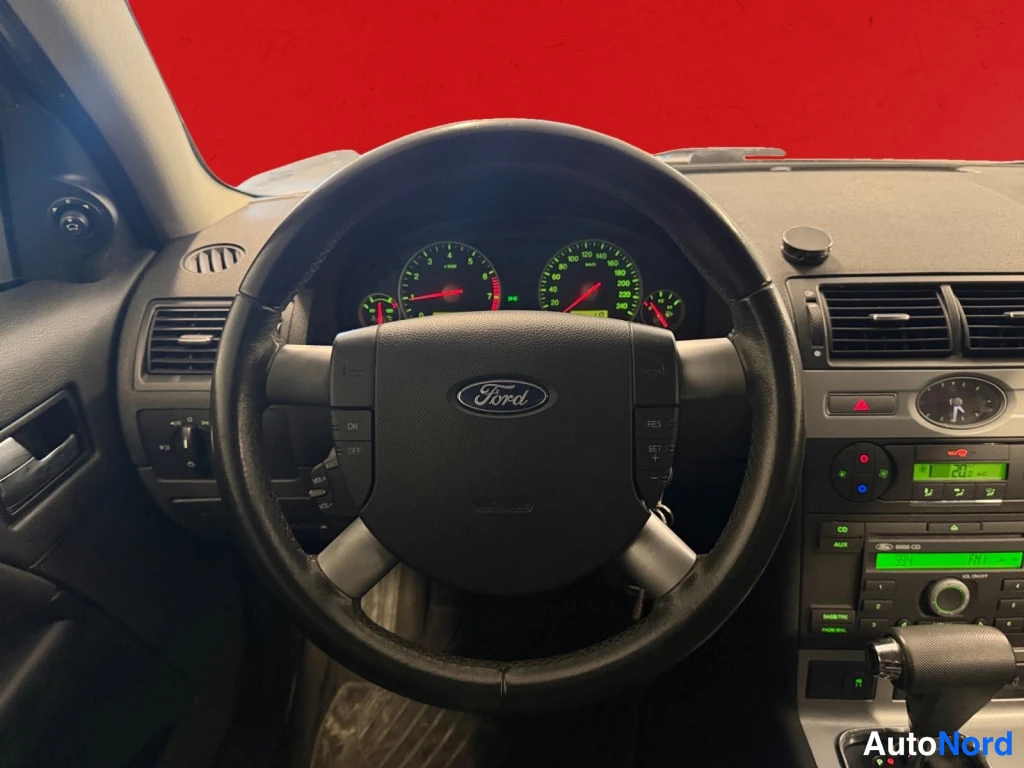 Yksityiskohta: Kuljettajan näkökulma ohjaamoon: Ford-merkillä varustettu ohjauspyörä, mittaristo ja kojelauta, jolla radio ja ilmastointilaitteet.
