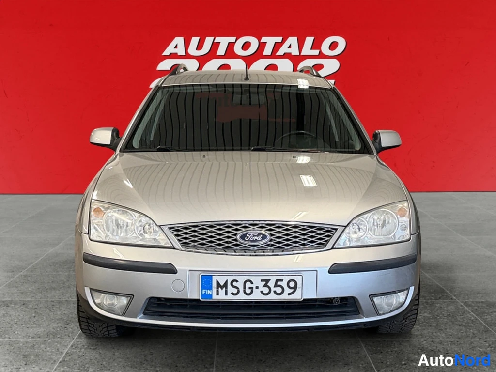 Edestä: Hopeanvärinen Ford Mondeo -asema-auto suoraan edestäpäin, Ford-merkki ja rekisterikilpi näkyvät punaisella taustalla.