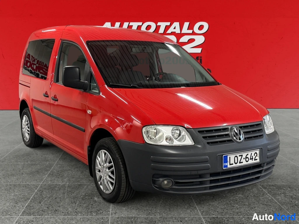 Etuviisto, nokka oikealle: Punainen Volkswagen Caddy etuosa ja vasen kylki kuvattuna edestä oikealta, rekisterikilpi.