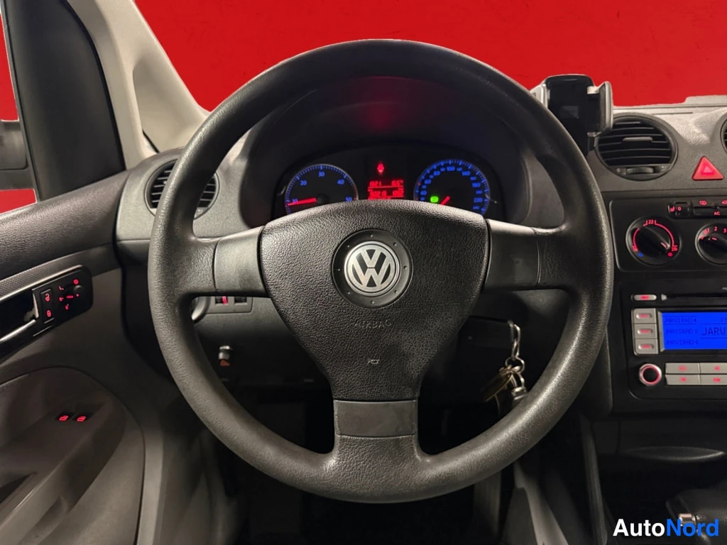 Muu: Ohjauspyörä ja mittaristo Volkswagenin sisätiloissa, punainen tausta.