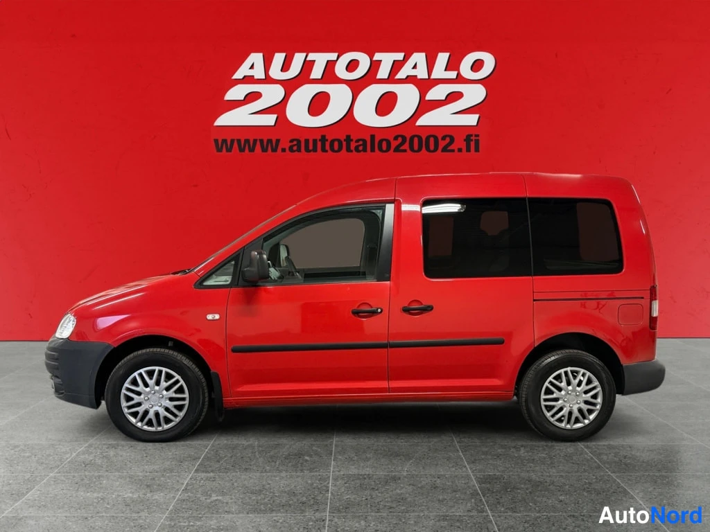 Etuviisto, nokka vasemmalle: Punainen Volkswagen Caddy -pakettiauto sivulta, keula hieman kohti kuvan vasenta reunaa.