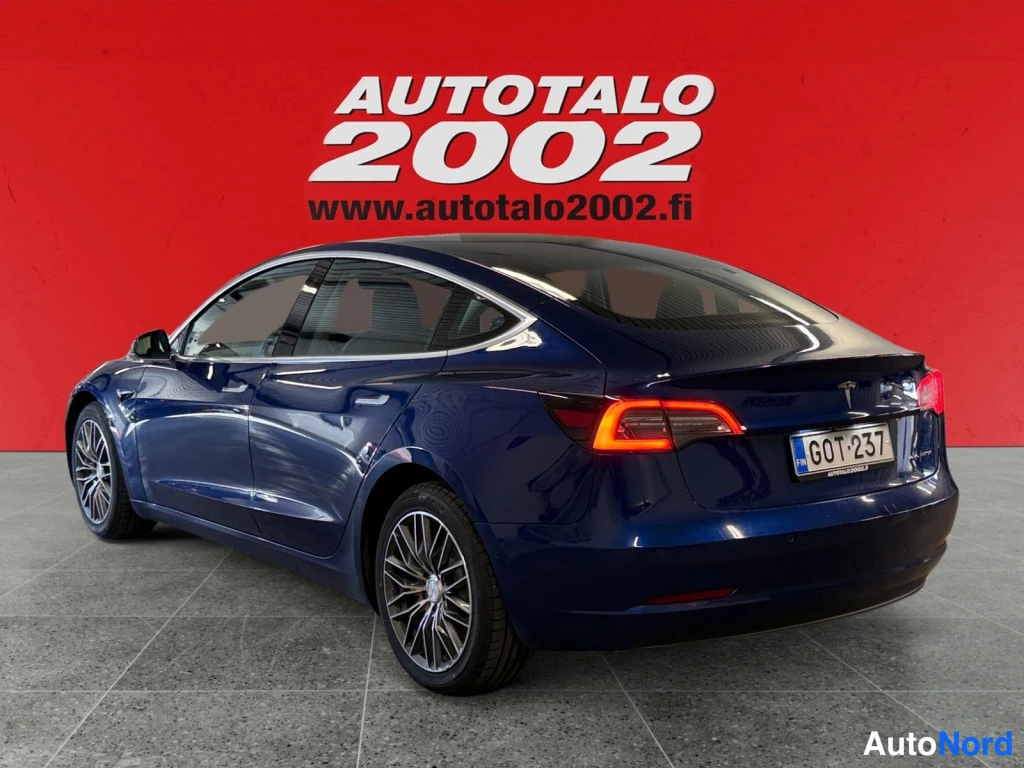 Takaviisto: Takakulmakuvassa tummansininen Tesla Model 3 rekisterikilvellä punaisella taustalla.