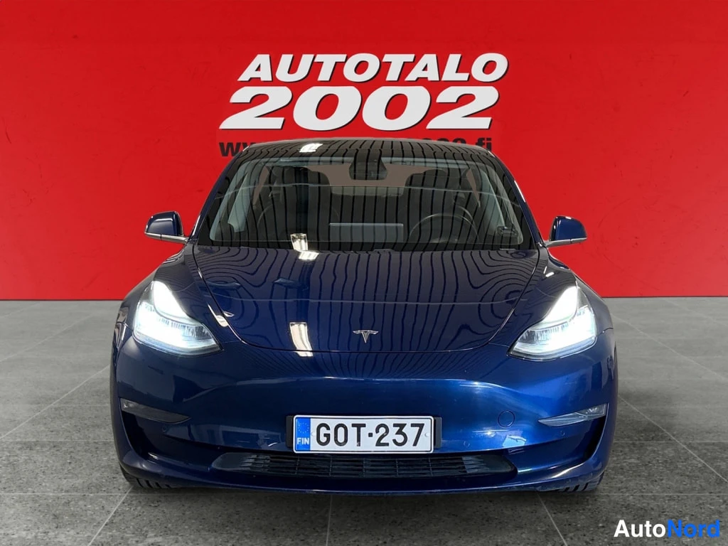 Edestä: Etukuvassa tummansininen Tesla Model 3 rekisterikilvellä punaisella taustalla.