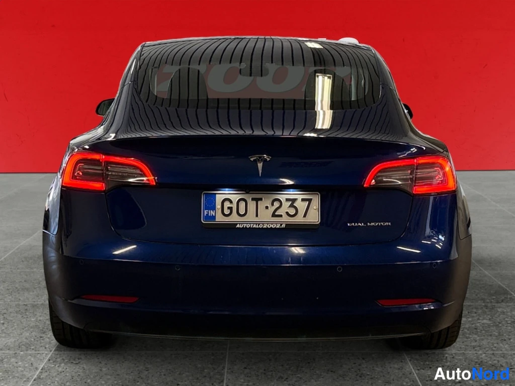 Takaa: Takakuvassa tummansininen Tesla Model 3 rekisterikilvellä punaisella taustalla, takakannessa Dual Motor -teksti.