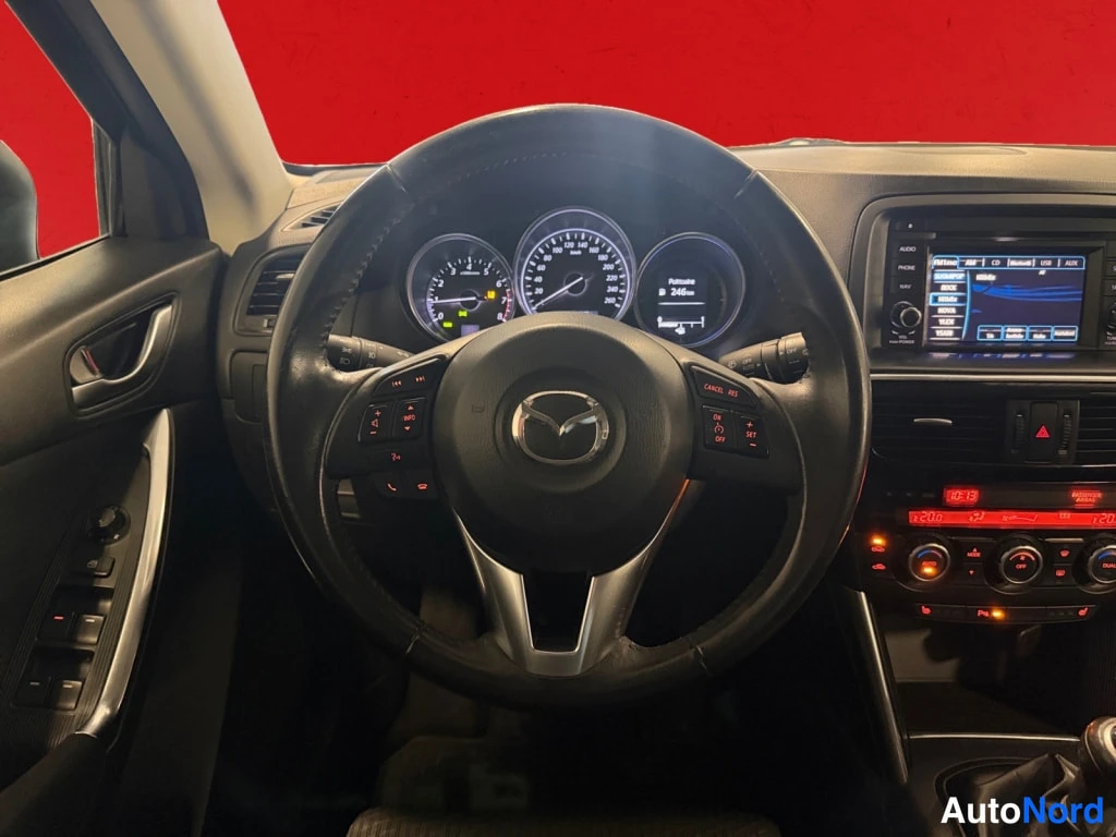 Muu: Ohjaamo Mazda-ohjauspyörällä: kojetaulun mittarit näkyvät, tietoviihdenäyttö ja radio keskikonsolissa, vaihdeton näkymä ratin takana.