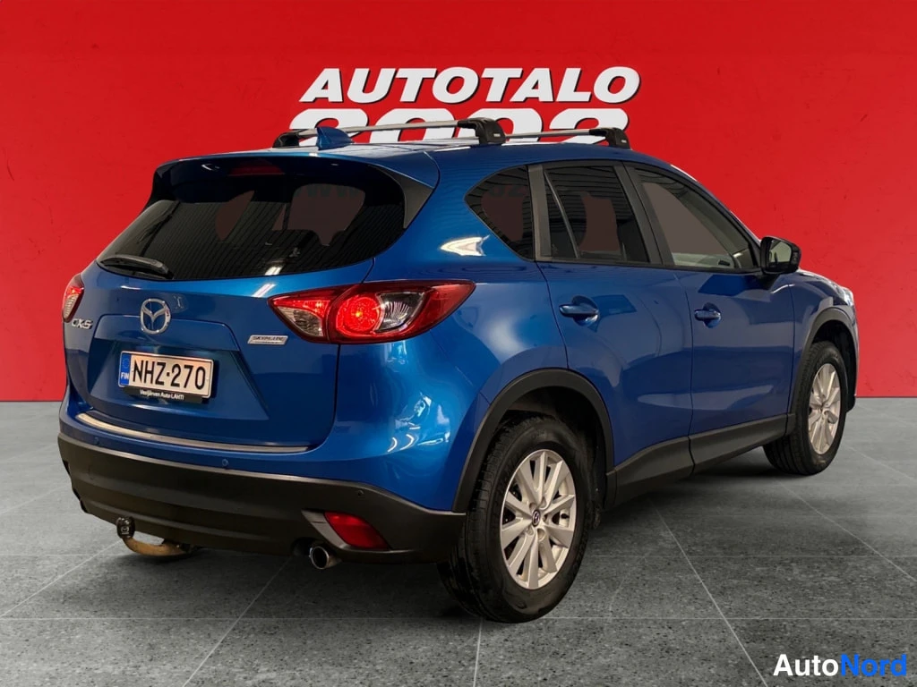 Takaviisto: Sininen Mazda CX-5 takaviistosta vasemmalta, rekisterikilpi ja vetokoukku näkyvissä.