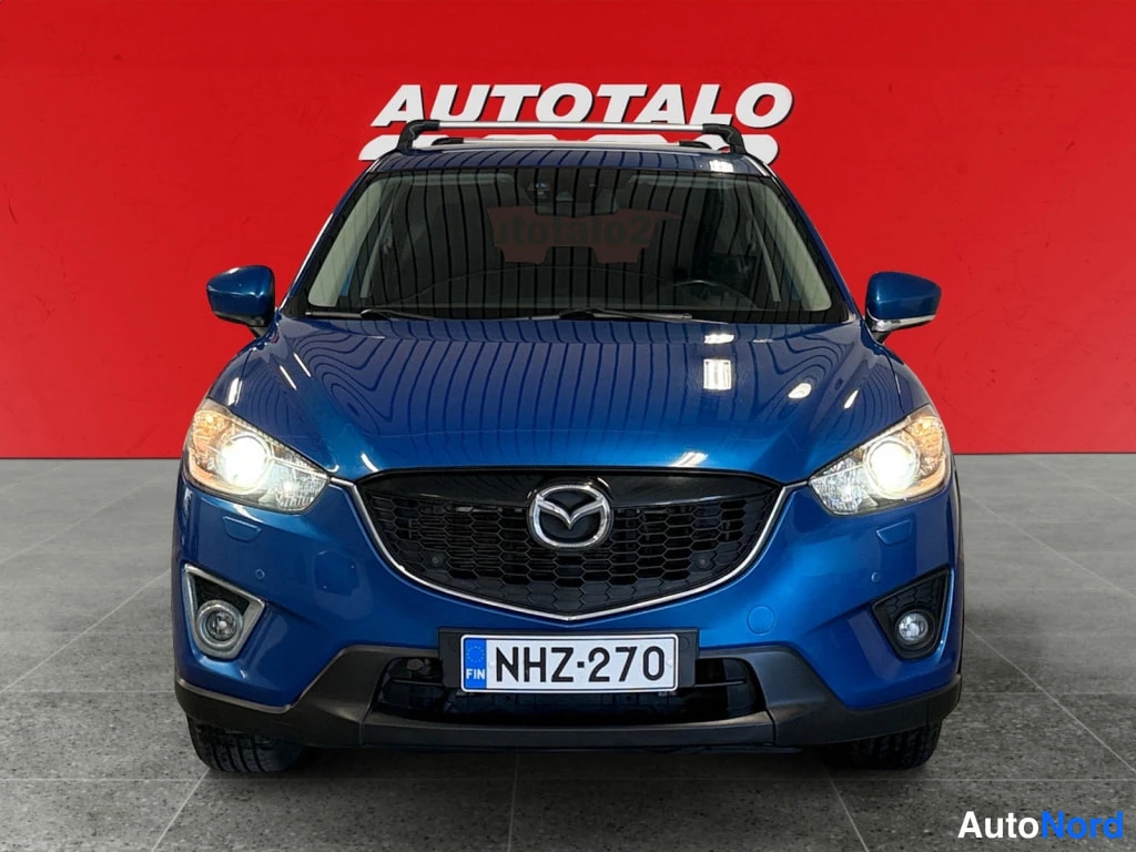 Edestä: Sininen Mazda CX-5 edestäpäin; etupuskurissa rekisteritunnus ja sumuvalot.