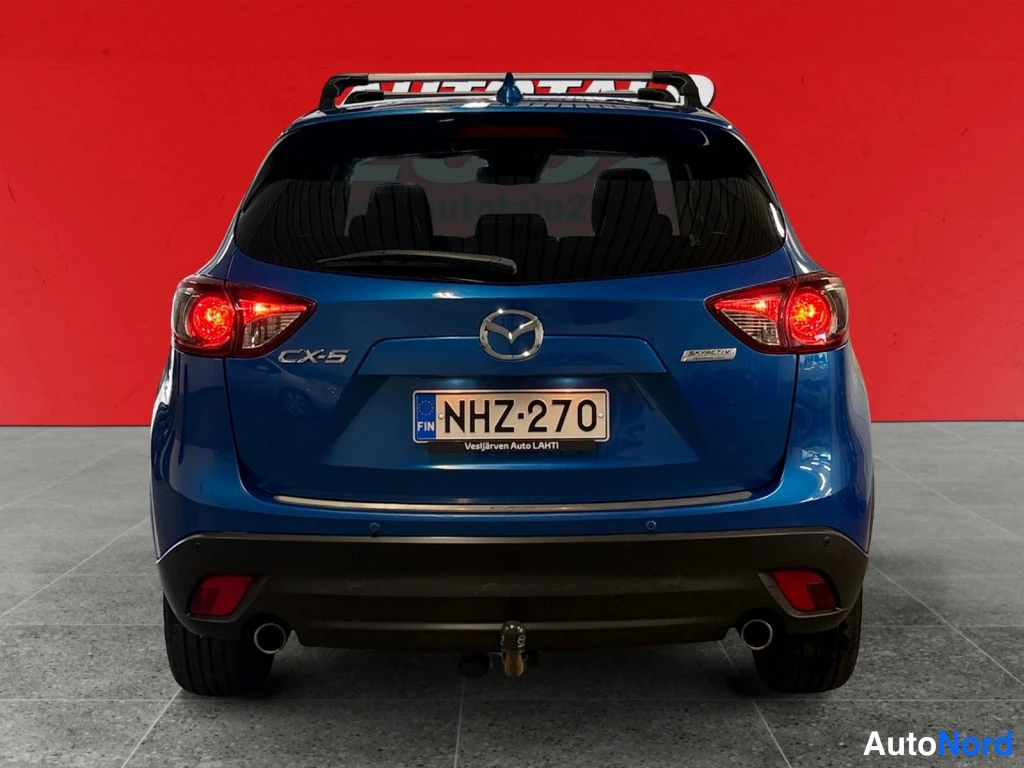 Takaa: Sininen Mazda CX-5 suoraan takaa; rekisteritunnus, CX-5-merkintä, kattoteline ja takahana.