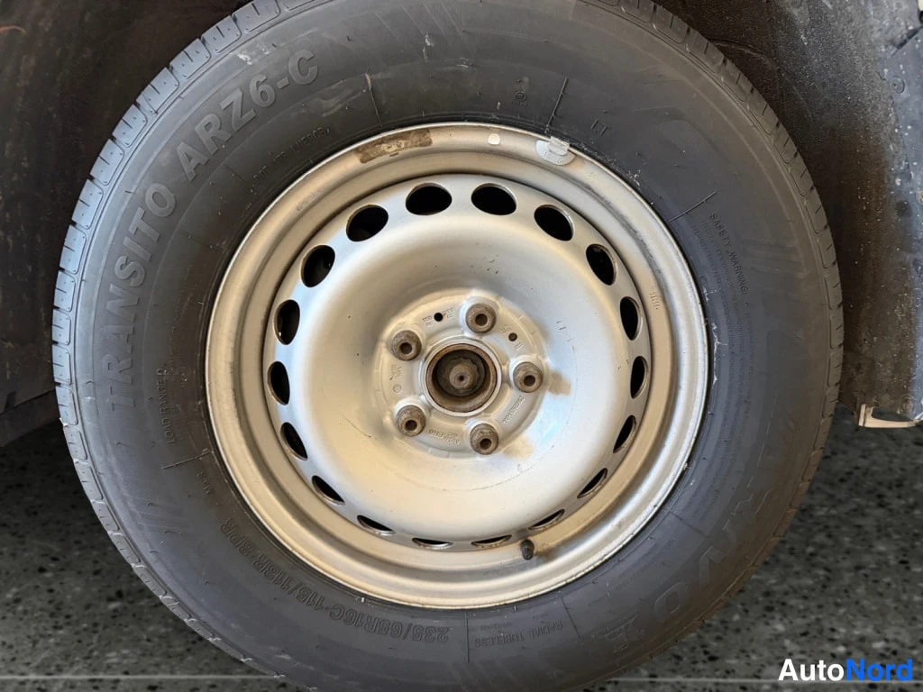 Muu: Lähikuva auton renkaasta ja teräsvanteesta, renkaan sivussa teksti TRANSITO ARZ6-C ja 235/65R16C 116/113R.