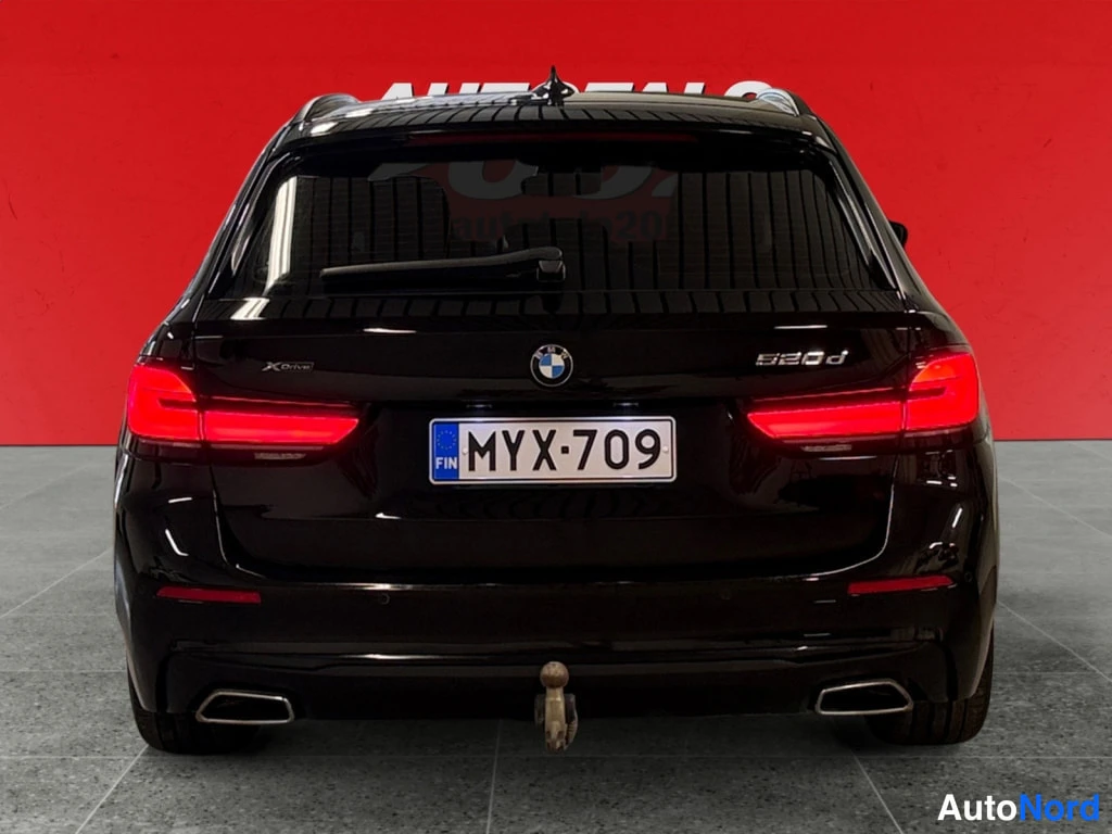 Takaa: Musta BMW:n takapää suoraan takaa, 520d-merkintä, rekisteritunnus, punainen tausta.