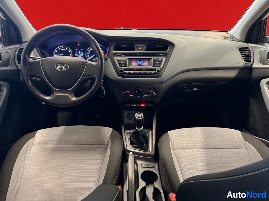 Muu: Näkymä kojelautaan istuimilta: Hyundai-ohjauspyörä, mittaristo, radio näytöllään 12:48, kolme kiertoilmaisinvalitsinta ja manuaalivaihteiston vaihdekeppi.