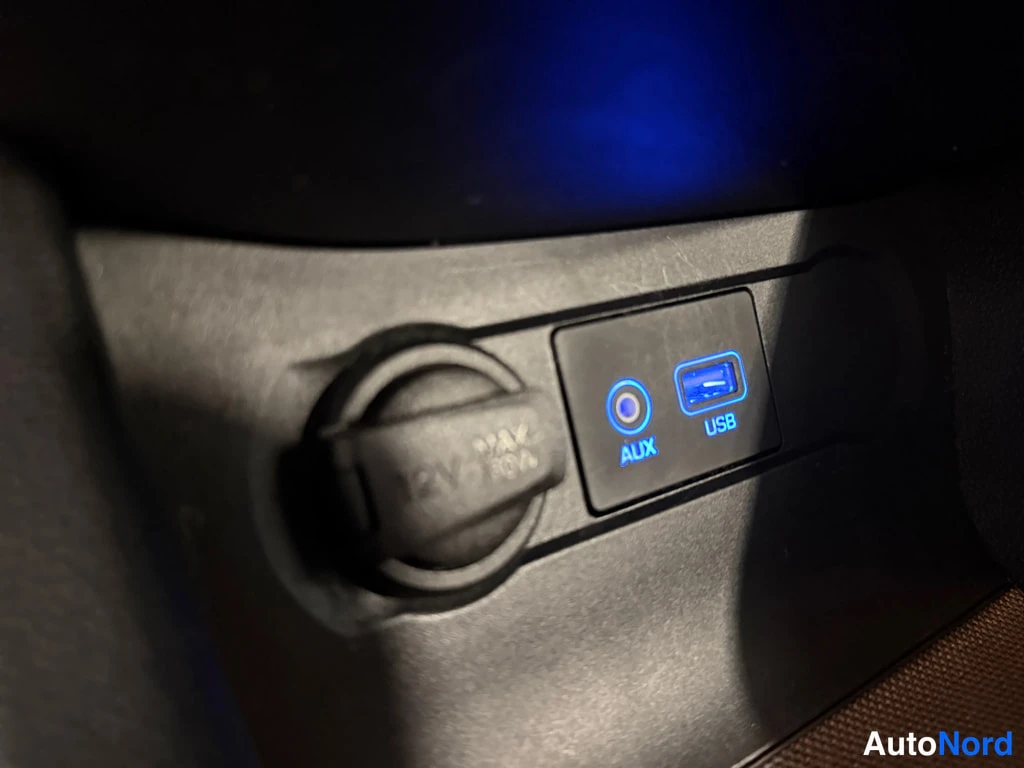 Muu: Lähikuva kojelaudan alapuolella: 12V-pistorasia kansilla (merkintä '12V 120W') sekä AUX- ja USB-portit sinisellä taustavalolla.