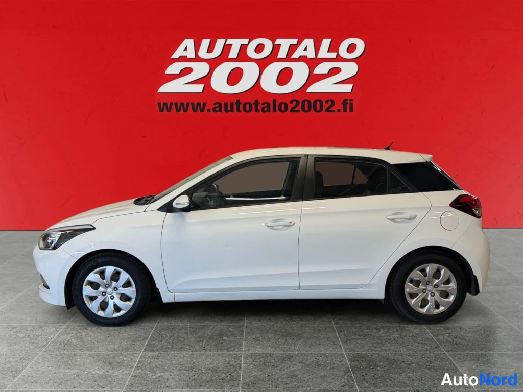 Etuviisto, nokka vasemmalle: Valkoinen Hyundai i20 -viistoperä auto sivulta etukulmasta, keula vasemmalla.