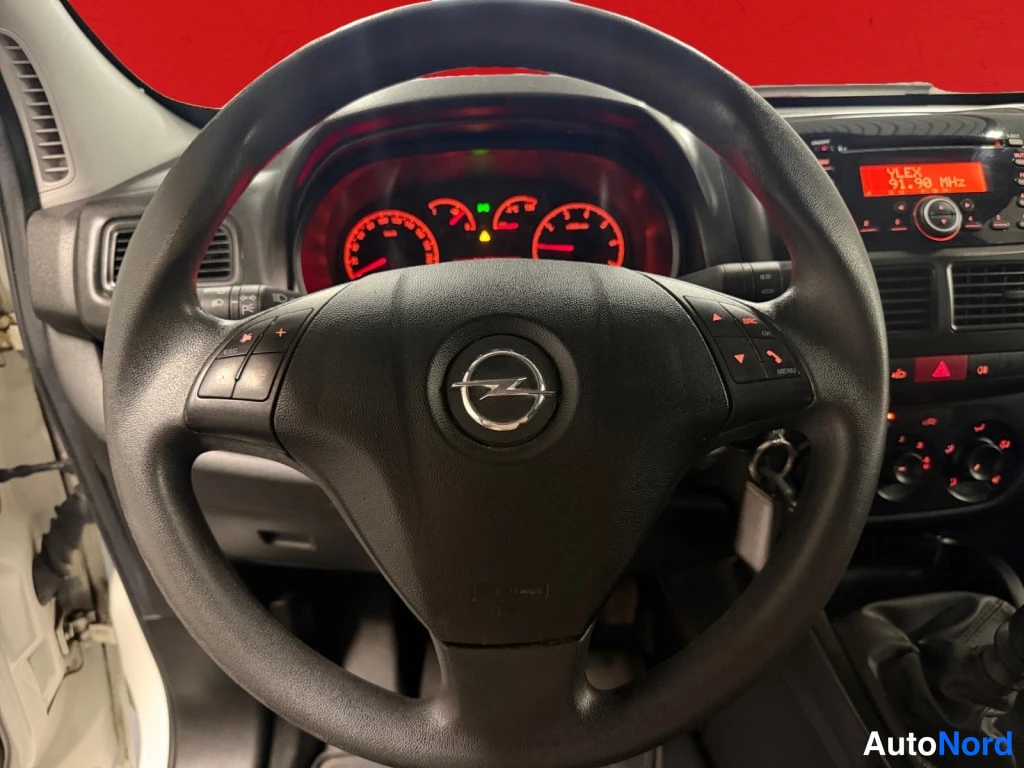 Yksityiskohta: Ohjauspyörä ja kojelauta: Opel-merkki ohjauspyörässä, punaiset mittarit ja radiopaneeli, joka näyttää tekst'in YLEX 91.90 MHz.