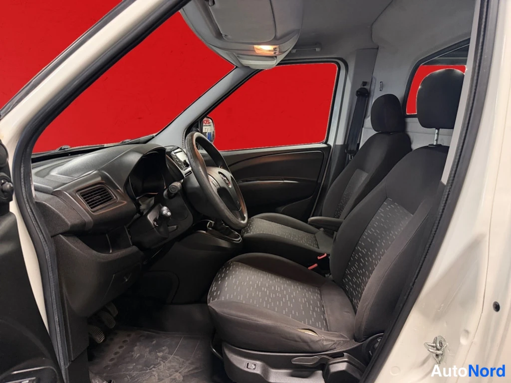 Yksityiskohta: Auton sisätilat kuljettajan ovesta katsottuna: tummat kankaistuolit, Opel-ohjauspyörä ja tumma kojelauta, punainen tausta.