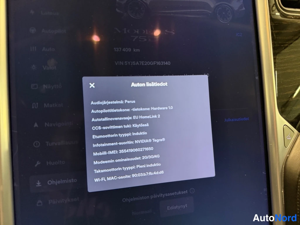 Edestä: Tesla infotainment dashboard dialog 'Auton lisätiedot' näyttää audiojärjestelmän 'Perus', Autopilot Hardware 1.0, HomeLink 2, CCS-tuen käytössä, induktiotakamoo