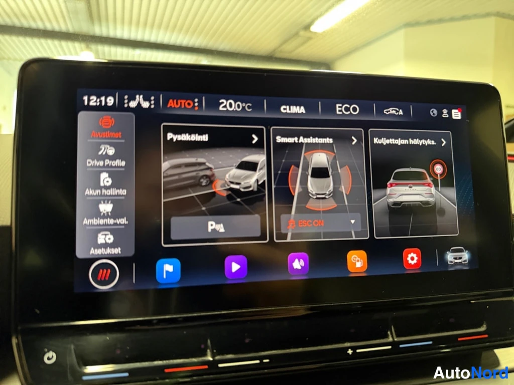 Yksityiskohta: Kojelaudan infotainment-näyttö, jossa näkyy ajoturvallisuus- ja assistenssiasetukset (Pysäköinti, Smart Assistants, Kuljettajan hälytykset).