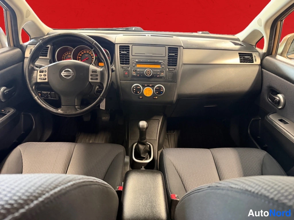 Yksityiskohta: Kojelauta ja etuistuimet takaa päin kuvattuna: Nissan-ohjauspyörä, radio, manuaalivaihdevipu ja käsijarru.