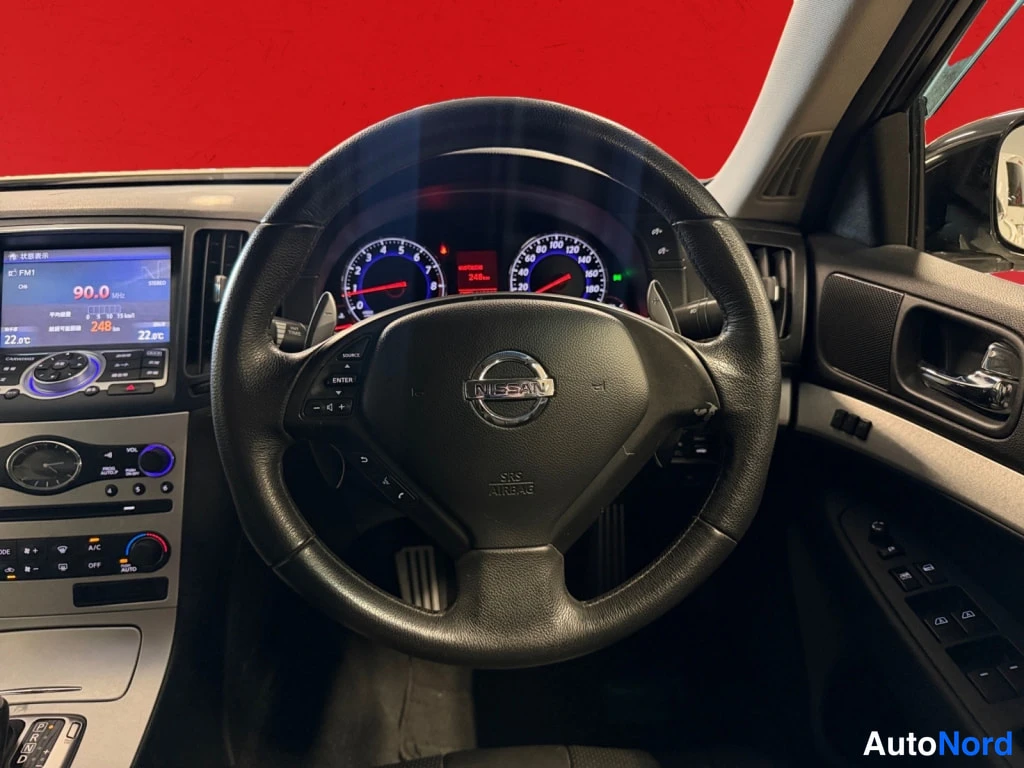 Muu: Ohjaamon näkymä: Nissan-merkkinen ohjauspyörä, mittaristo ja keskikonsolin näyttö, jonka radiossa lukee 90.0 MHz FM1.