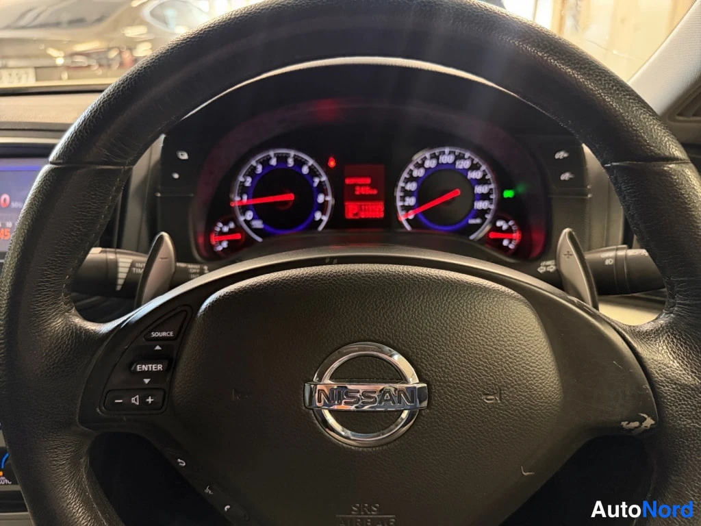 Muu: Nissan-ohjauspyörän takaa kuvattu mittaristo: tehomittari ja nopeusmittari punaisilla neuloilla, keskellä punainen digitaalinäyttö, NISSAN-logo ohjauspyörässä.