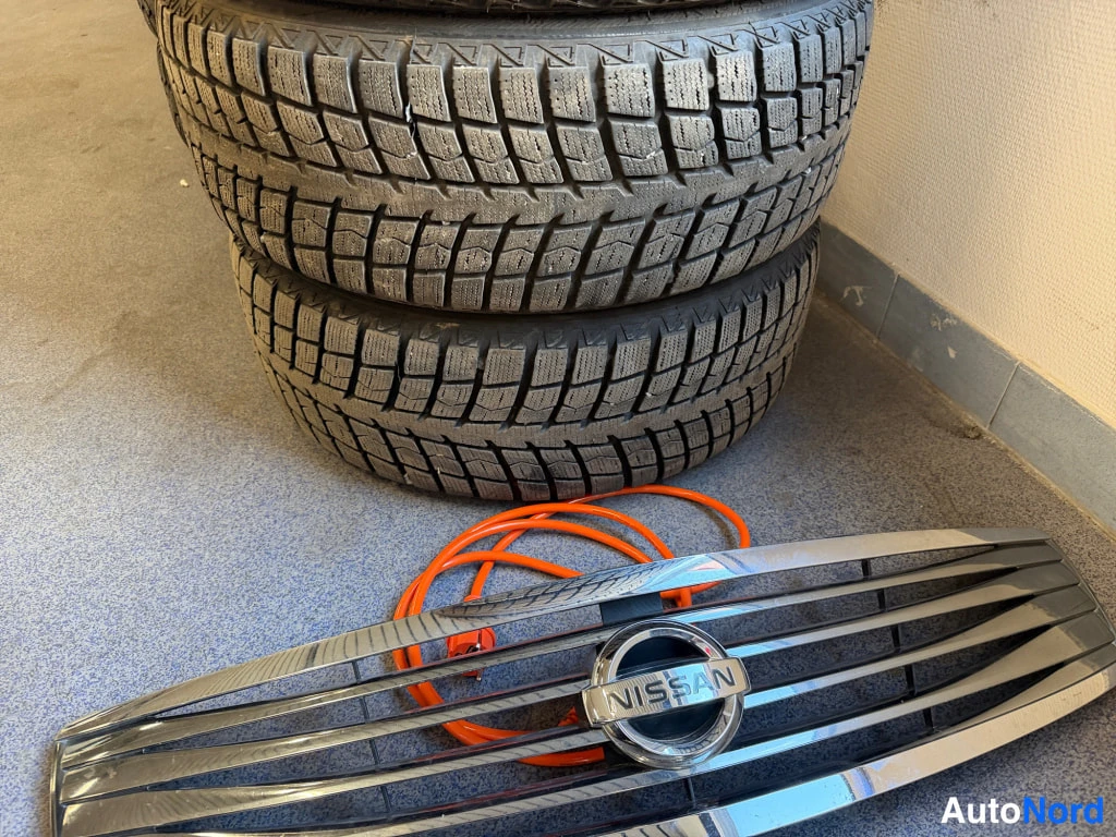 Yksityiskohta: Pino talvirenkaita ja Nissan-merkillä varustettu irrotettu etusäleikkö lattialla.