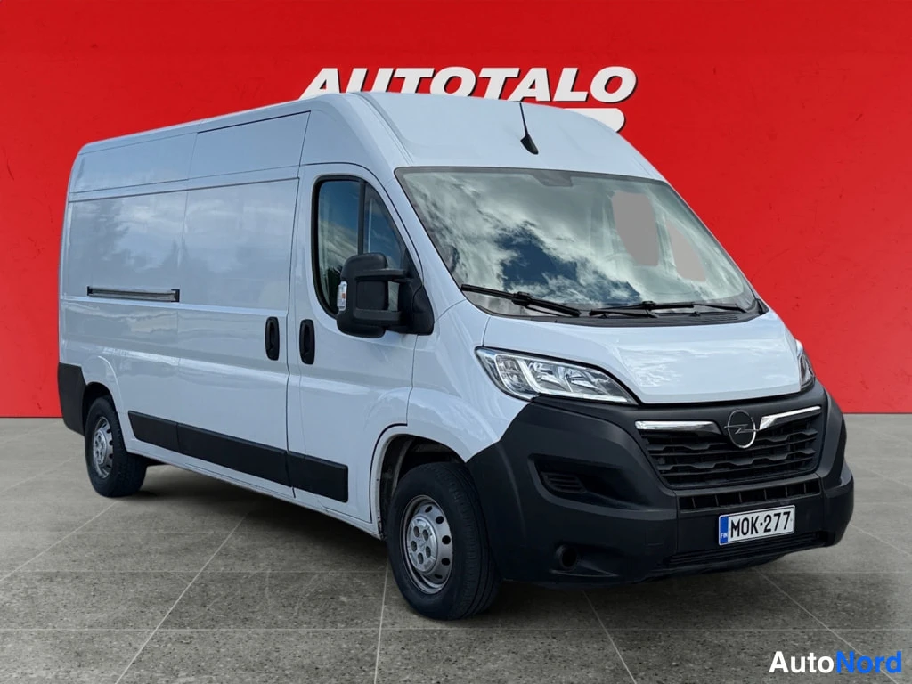Etuviisto, nokka oikealle: Valkoisen Opel Movano -pakettiauton etukulmanäkyvä auto, etusäleikkö ja ajovalot näkyvät, rekisterikilpi.