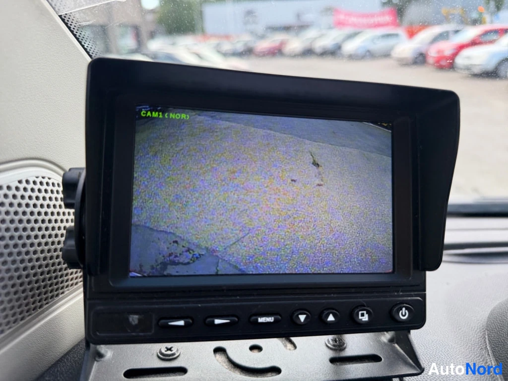 Muu: Kojelaudassa kiinnitetty peruutuskamera-näyttö, jonka ruudulla teksti CAM1 (NOR) ja kuva parkkialueelta.