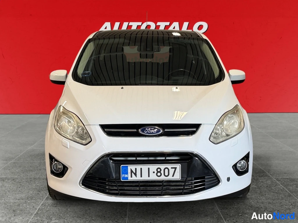 Edestä: Valkoisen auton etukuva suoraan edestä, Ford-merkki ja rekisterikilpi näkyvät etusäleikössä.