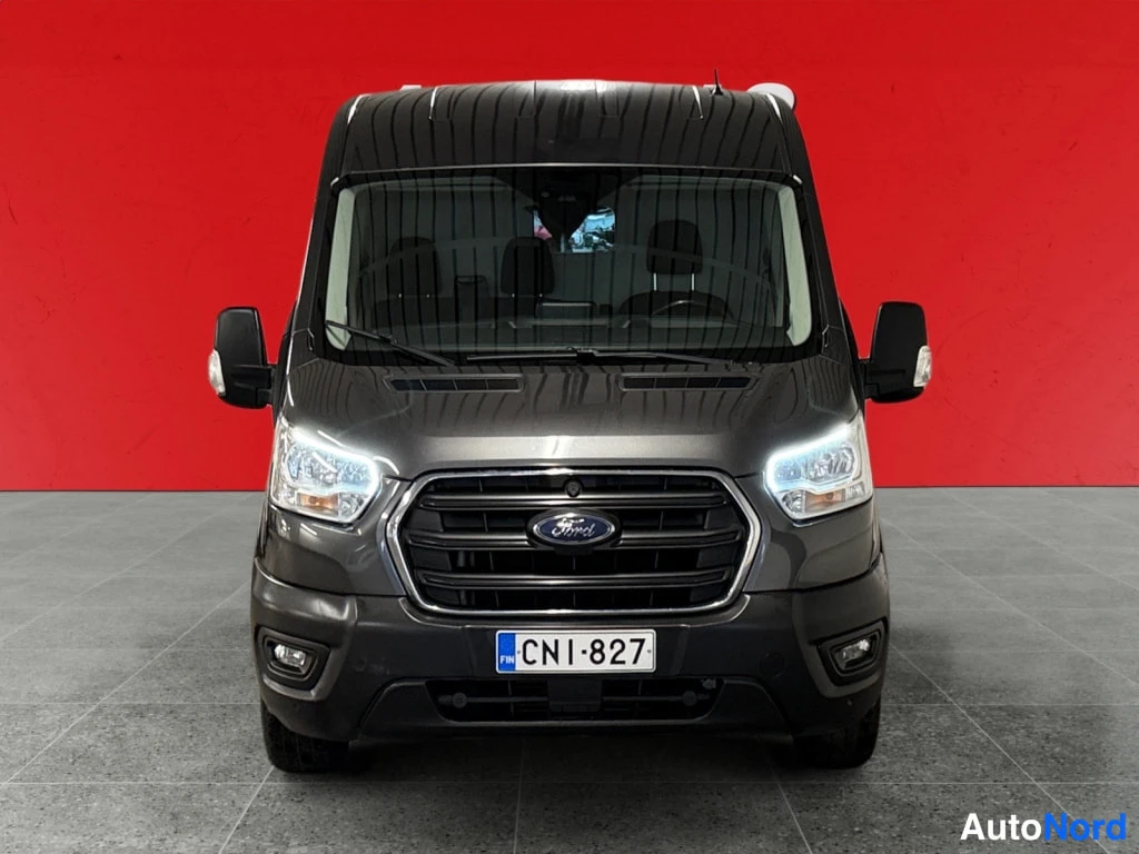 Edestä: Ford Transit -pakettiauton etunäkymä punaisella taustalla; etusäleikkö, Ford-merkki ja rekisterikilpi näkyvät.